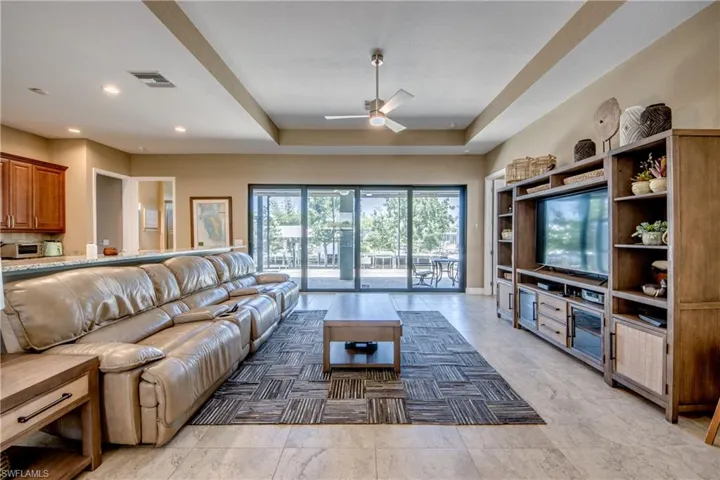 Living room featuring ceiling fan, a raised ceiling, and light tile patterned flooring