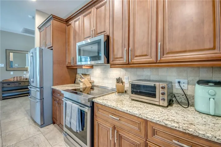 Kitchen with light stone counters, appliances with stainless steel finishes, light tile patterned floors, and backsplash