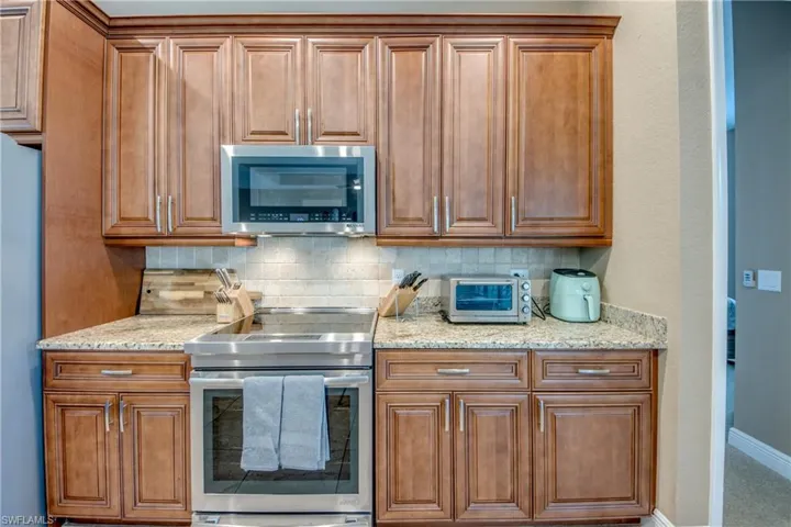 Kitchen with decorative backsplash, carpet flooring, stainless steel appliances, and light stone countertops