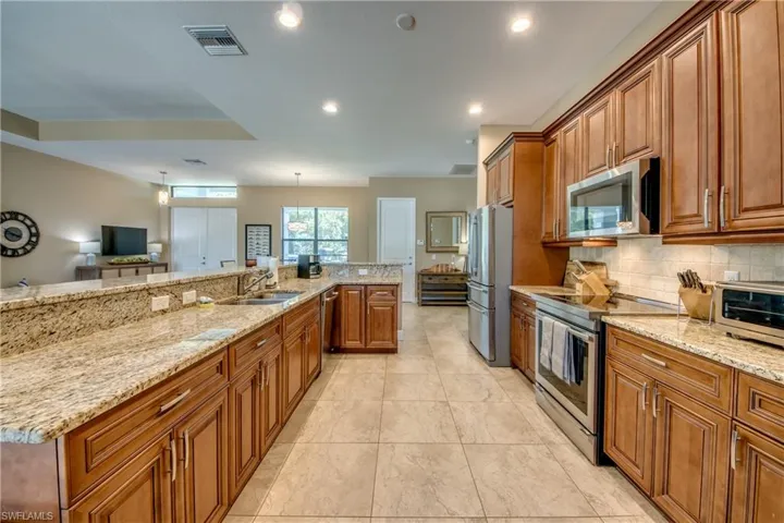 Kitchen with light tile patterned flooring, appliances with stainless steel finishes, sink, and light stone countertops