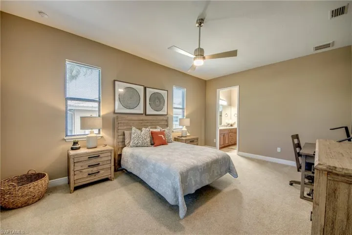 Bedroom with ceiling fan, connected bathroom, light colored carpet, and multiple windows