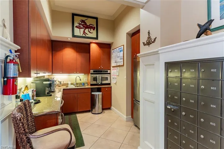 Kitchen with ornamental molding, light stone countertops, appliances with stainless steel finishes, light tile patterned flooring, and mail area