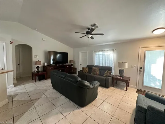 Living room with vaulted ceiling, a healthy amount of sunlight, light tile patterned floors, and ceiling fan