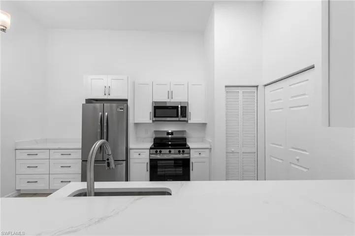 Modern kitchen featuring white shaker cabinetry, stainless steel appliances, white countertops, and a prominent kitchen island with an undermount sink