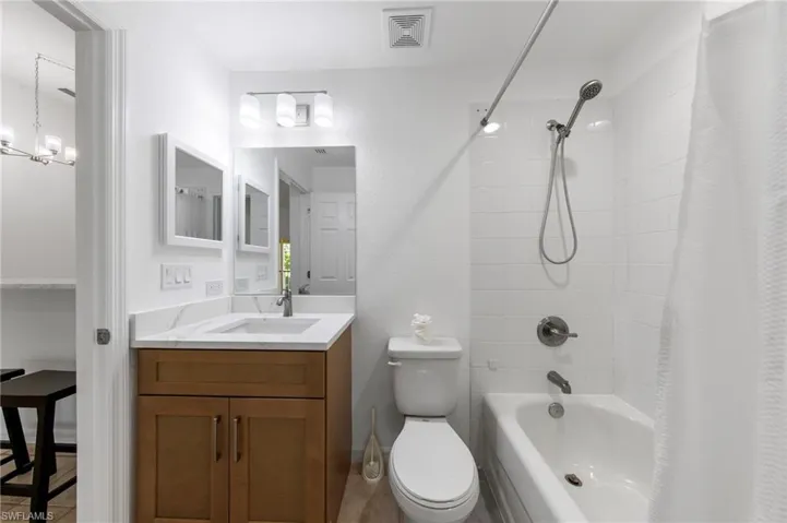 Bathroom featuring a wood-finish vanity with a white countertop, an undermount sink, a large wall mirror, and a tiled tub/shower combination