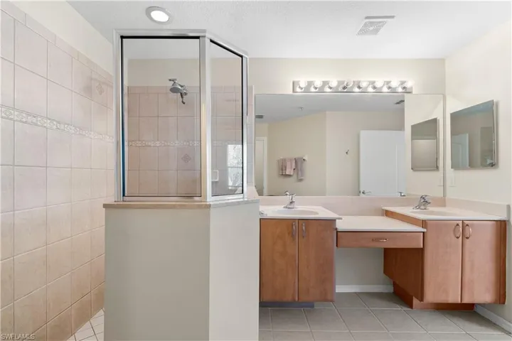 Bathroom with a shower with shower door, tile flooring, oversized vanity, and dual sinks