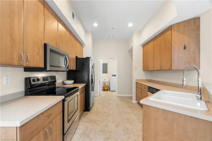 Kitchen with appliances with stainless steel finishes, sink, washer / clothes dryer, and light tile floors