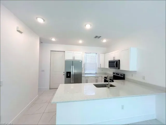 Kitchen with light stone counters, white cabinetry, stainless steel appliances, light marble finish floors, and a peninsula