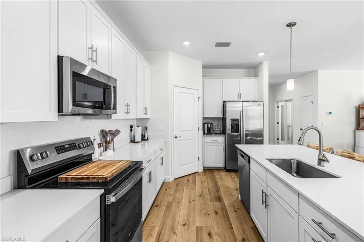 Kitchen featuring stainless steel appliances, white cabinets, pendant lighting, backsplash, and light stone counters