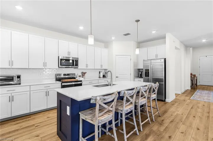 Kitchen with white cabinetry, appliances with stainless steel finishes, hanging light fixtures, decorative backsplash, and recessed lighting