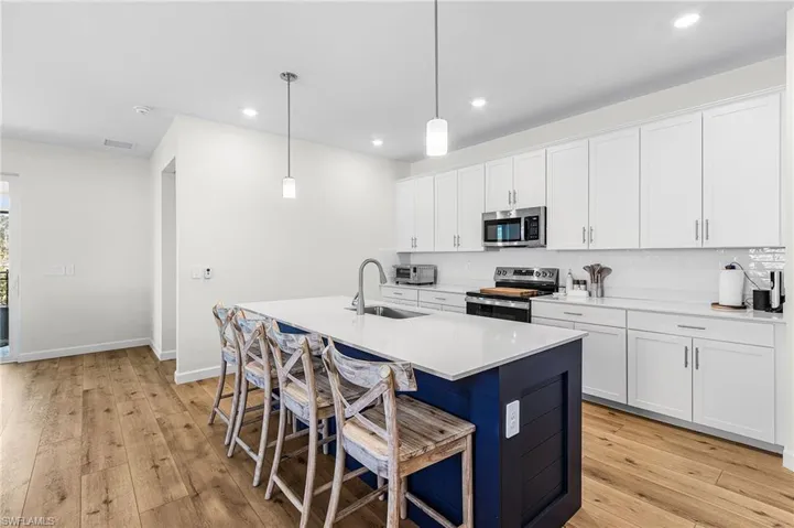 Kitchen featuring white cabinetry, pendant lighting, an island with sink, a breakfast bar, and stainless steel appliances