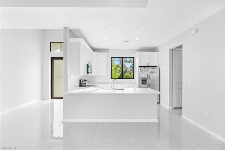 Kitchen featuring white cabinets, appliances with stainless steel finishes, light stone counters, a peninsula, and backsplash