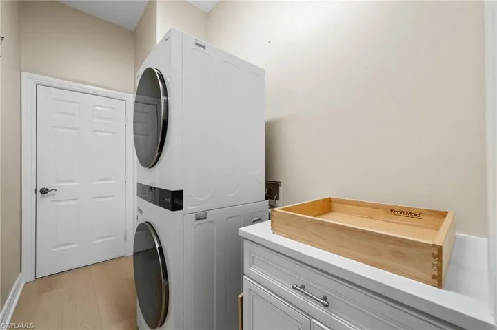 Laundry room featuring new stackable washer and dryer, light wood-style tile floors, and wash tub