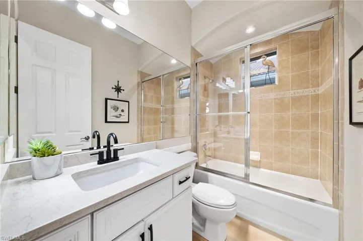 Full bathroom featuring hardwood / wood-style floors, combined bath / shower with glass door, toilet, and vanity