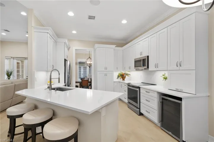 Kitchen featuring wine cooler, white cabinets, light hardwood / wood-style floors, appliances with stainless steel finishes, under-cabinet lighting and sink