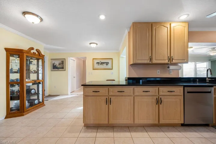 Kitchen with crown molding, dishwasher, light wood finish cabinetry, light tile patterned flooring, and dark stone countertops