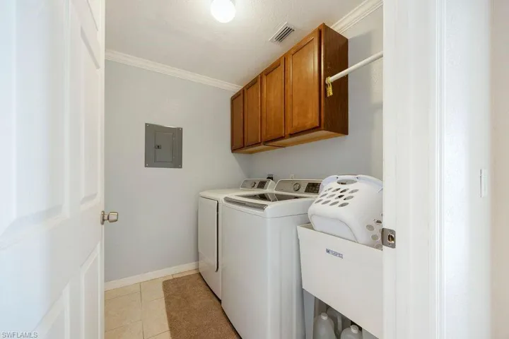 Laundry room featuring electric panel, crown molding, cabinet space, washing machine and clothes dryer, and light tile patterned floors