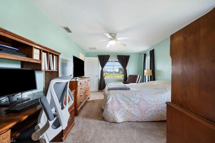 Bedroom with light colored carpet, an office area, and a ceiling fan