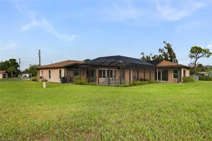 Rear view of property with a sunroom, a lanai, a lawn, and stucco siding