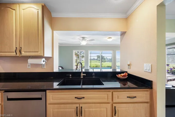 Kitchen featuring light wood finish cabinetry, ornamental molding, dishwasher, dark stone countertops, and ceiling fan