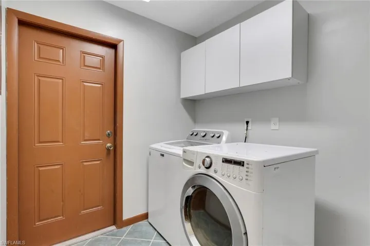 Laundry area with light tile patterned floors, cabinet space, and washing machine and clothes dryer