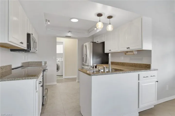 Kitchen featuring white cabinetry, light stone countertops, a tray ceiling, and a peninsula