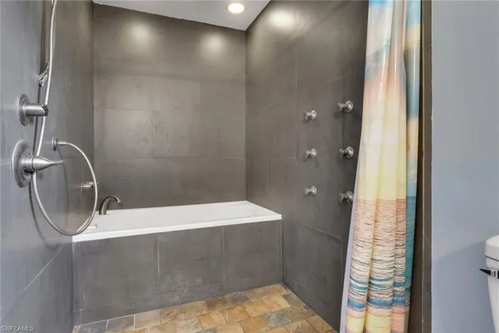 Bathroom featuring a tile shower, tile walls, stone finish flooring, and a relaxing tiled tub