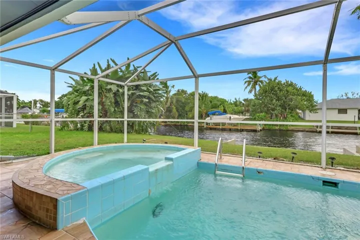 View of pool featuring a sunroom, a lawn, a water view, and a pool with connected hot tub