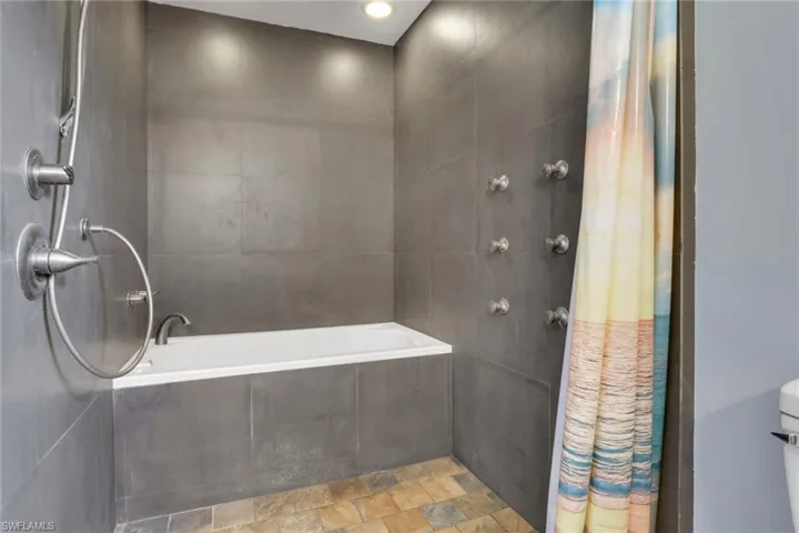Full bath featuring a tile shower, stone finish floors, tile walls, and tiled tub