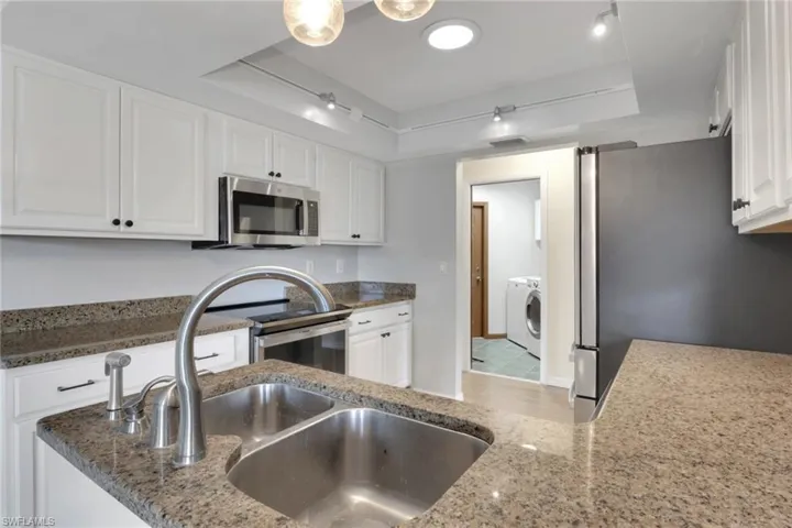 Kitchen with a tray ceiling, white cabinetry, dark stone counters, and stainless steel appliances