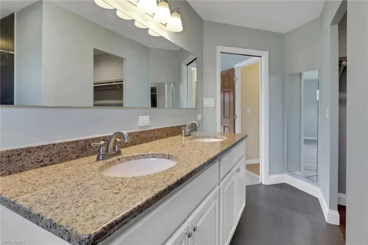 Full bath with a spacious closet, double vanity, a shower stall, and dark tile patterned flooring