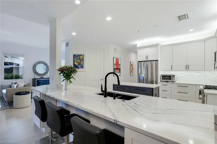 Kitchen with white cabinets, stainless steel refrigerator with ice dispenser, light stone counters, and sink