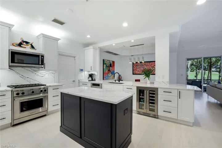 Kitchen with white cabinets, decorative light fixtures, kitchen peninsula, stainless steel appliances, and beverage cooler