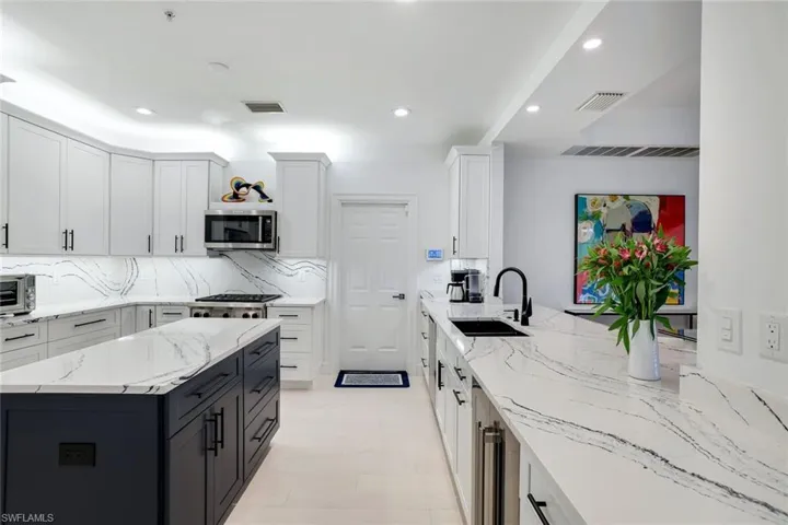 Kitchen featuring white cabinetry, sink, light stone countertops, tasteful backsplash, and appliances with stainless steel finishes