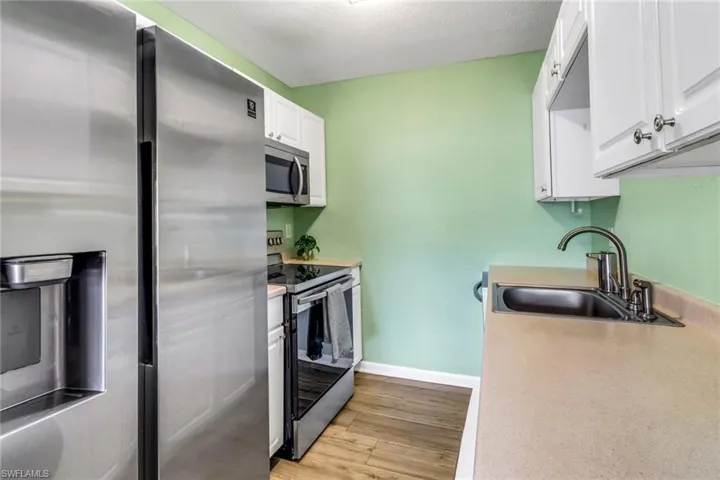 Kitchen with appliances with stainless steel finishes, light countertops, light wood-style flooring, white cabinetry, and a textured ceiling