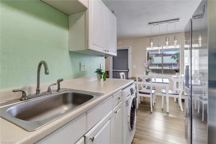 Kitchen with stainless steel fridge, light countertops, white cabinetry, washer / clothes dryer, and light wood-style flooring