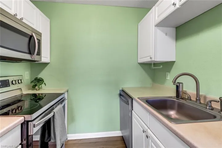 Kitchen with appliances with stainless steel finishes, white cabinetry, light countertops, and dark wood-type flooring
