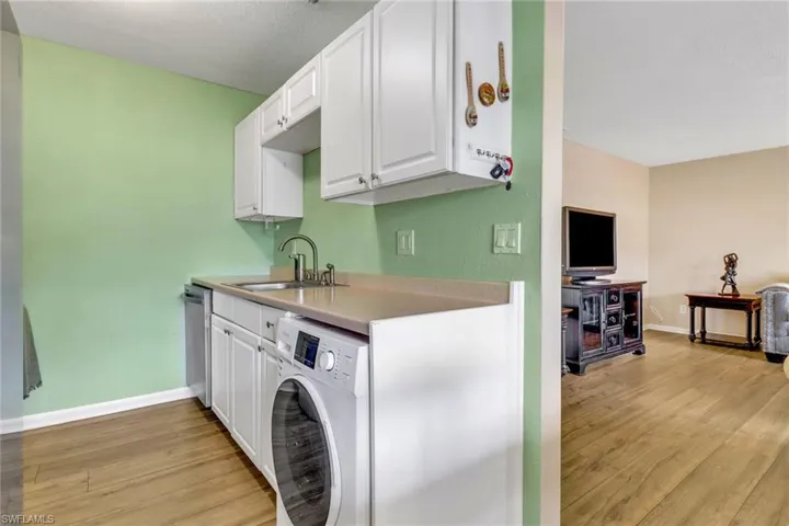 Kitchen featuring white cabinets, light wood-style flooring, washer / clothes dryer, and light countertops