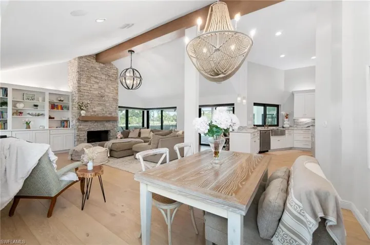 Dining space with a stone fireplace, light wood-style flooring, hanging lights, and lofted ceiling