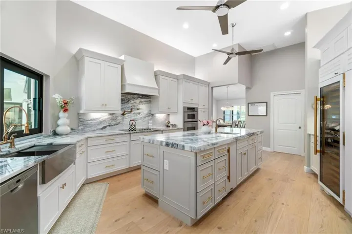 Kitchen with stainless steel appliances, light stone countertops, beverage cooler, gray cabinets, and lofted ceiling