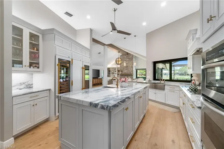 Kitchen featuring stainless steel appliances, light stone counters, glass insert cabinets, gray cabinetry, and beverage cooler