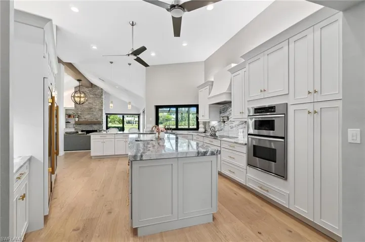 Kitchen with double oven, white cabinetry, light stone countertops, light wood-style floors, and hanging light fixtures