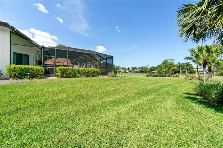 View of grassy yard featuring glass enclosure and a sunroom