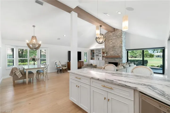 Kitchen featuring hanging lights, light stone countertops, dishwasher, and a stone fireplace
