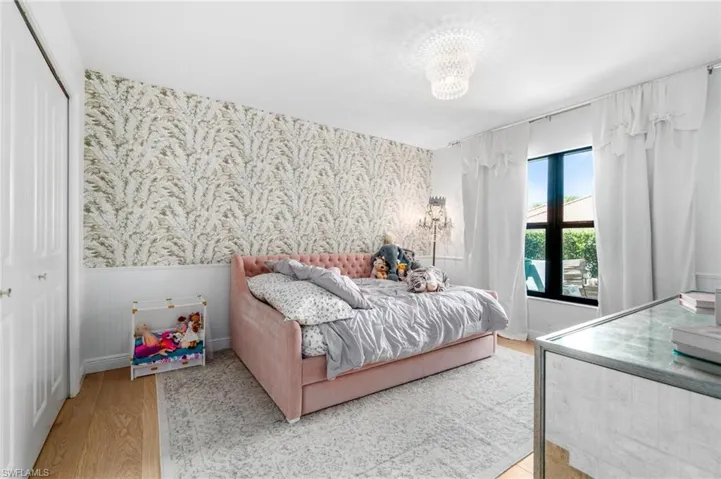 Bedroom featuring light wood-style flooring, a closet, wainscoting, wallpapered walls, and a chandelier