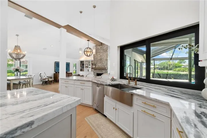 Kitchen with a chandelier, light stone countertops, stainless steel dishwasher, and lofted ceiling