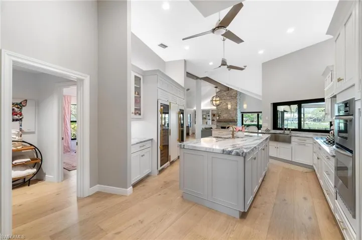 Kitchen with a high ceiling, glass fronted cabinets, light stone countertops, light wood-style floors, and decorative light fixtures