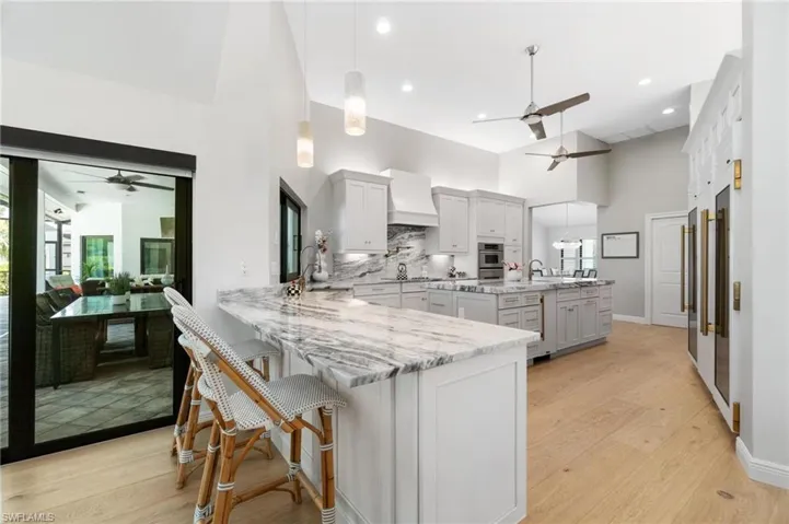 Kitchen with a ceiling fan, a breakfast bar area, decorative light fixtures, light wood-style flooring, and a high ceiling