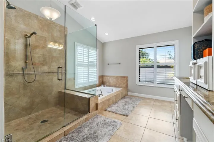 Full bath featuring a garden tub, a shower stall, light tile patterned floors, lofted ceiling, and plenty of natural light