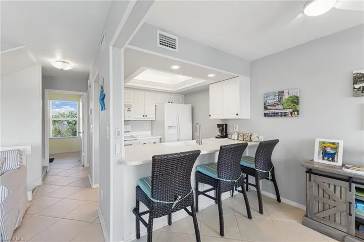 Kitchen featuring white cabinets, light countertops, a kitchen bar, white appliances, and a raised ceiling